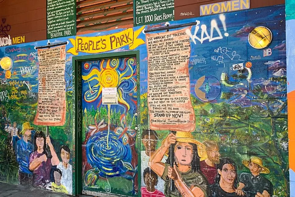 Colorful mural depicting people holding signs with proclamations on exterior wall of public restroom in People's Park, Berkeley